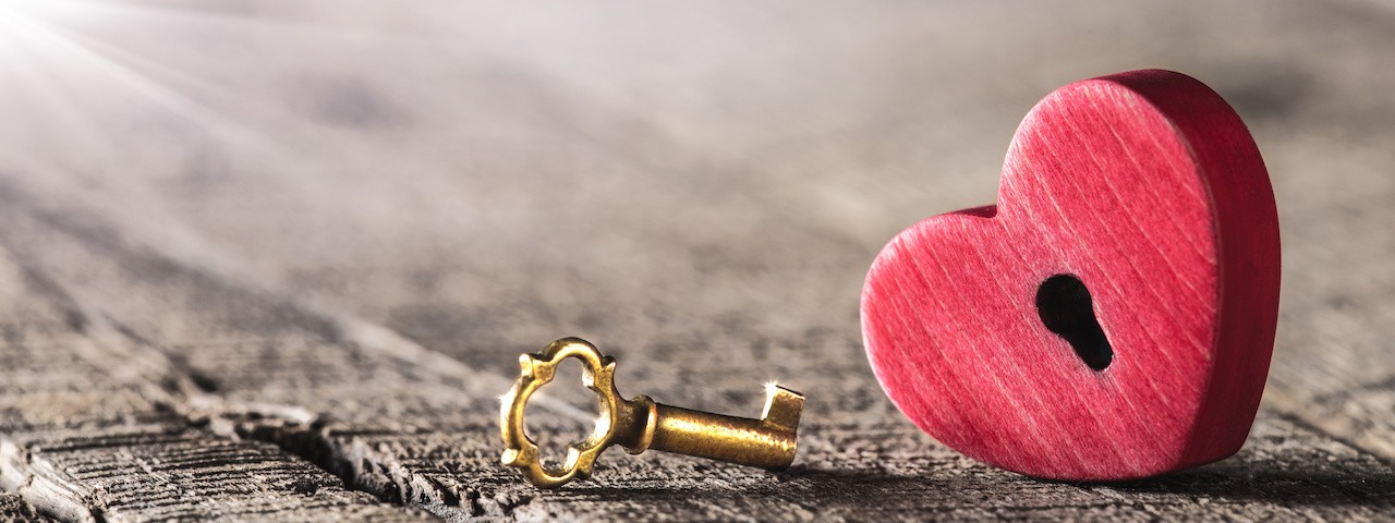 A wooden heart with a keyhole laid next to a golden key.